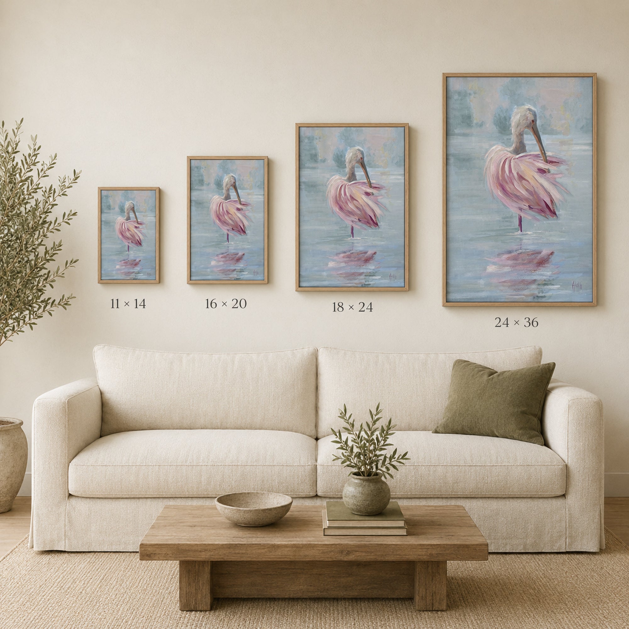 Four framed wall art prints showing pink spoonbill in a light blue water scene, displayed above a cream sofa in a styled living room. Size labels beneath each print read 11 x 14, 16 x 20, 18 x 24, and 24 x 36.