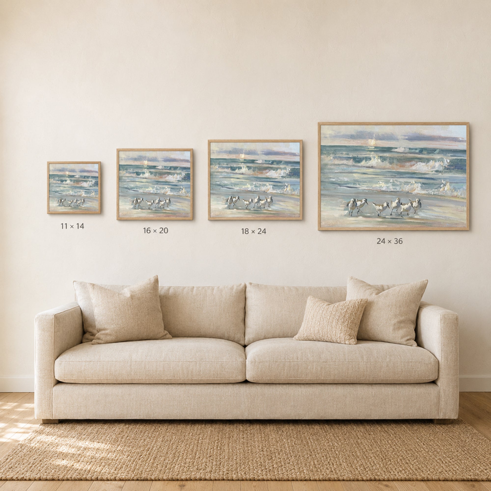 A staged living room scene showing a beige sofa beneath four framed ocean paintings of increasing size, with size labels printed below each frame.
