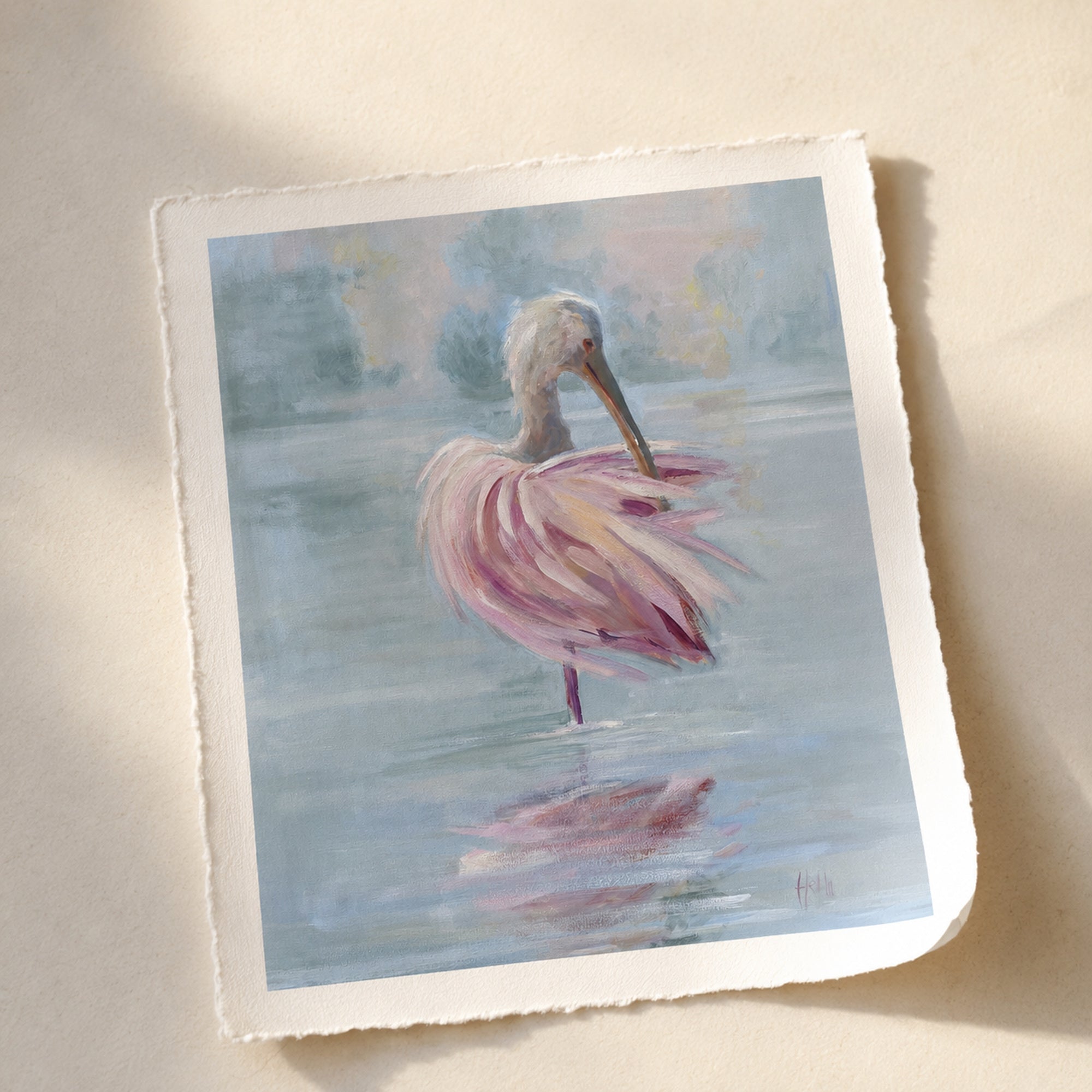 A square art print with torn paper edges featuring a pastel painting of a pink spoonbill standing in water, photographed on a light beige surface with soft shadows.