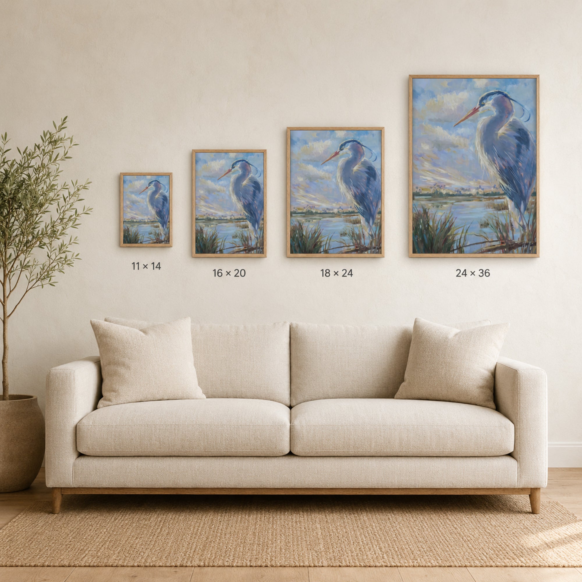 A staged interior scene showing a cream sofa against a light beige wall, with four framed heron paintings of increasing size mounted above the couch. Small size labels beneath the frames read 11 x 14, 16 x 20, 18 x 24, and 24 x 36.